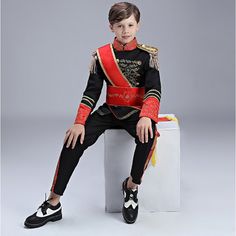 a young boy sitting on top of a white box wearing a red and black uniform