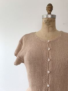 80s button down knit silk blend cap sleeves the perfect peach/taupe color scoop neck ribbed waist and sleeve cuffs a perfect layering piece for all year! small mother of pearl buttons Approx size S fabric has some stretch shoulders-16 lay flat inches Bust-35 inches Waist-28 inches Length-22.5 inches excellent condition era-80s label-Condor 55% silk 45% cotton Fitted Summer Sweater With Buttons, Summer Fitted Sweater With Buttons, Vintage Knitted Beige Tops, Vintage Beige Knitted Tops, Fitted Everyday Sweater With Buttons, Fitted Sweater With Buttons For Everyday, Everyday Fitted Sweater With Buttons, Stretch Shoulders, Taupe Sweater