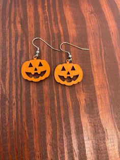 two carved pumpkins are hanging from earrings on a wooden table with wood grained surface