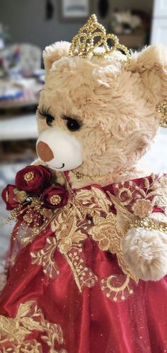 a teddy bear dressed in a red dress with gold trimmings and a tiara