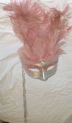 a masquerade mask with pink feathers on a white sheeted bed topper