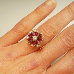 Here we have a gorgeous earth mined red ruby and sparkly white diamond 1950s ring in 14K yellow gold.This exceptional floral ring is gorgeous from every angle you view it- it's like a small wearable sculpture. The gem quality rubies are beautifully matched for color throughout. There are 0.81 carats of fine gem rubies. In total the diamond accents weigh 0.34 carats. These pretty diamonds are SI clarity and J in color. The total precious ruby and diamond weight here is 1.15 carats. Inside the sha Cluster Ruby Ring With Brilliant Cut Diamonds, Ruby Ring With Diamond Cluster And Brilliant Cut, Cluster Ruby Ring With Center Stone, Cluster Ruby Diamond Ring With Center Stone, Ruby Multi-stone Cluster Ring, Ruby Cluster Ring With Brilliant Cut, Cluster Ruby Diamond Ring, Red Ruby Cluster Ring With Rose Cut Diamonds, Fine Jewelry Ruby Ring With Cluster Halo Setting