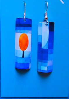 two blue and white earrings with an orange tree on them, against a blue background