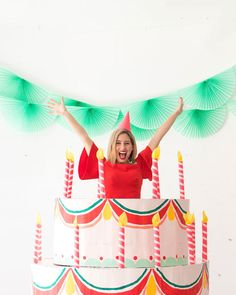 a woman standing on top of a birthday cake with her arms up in the air