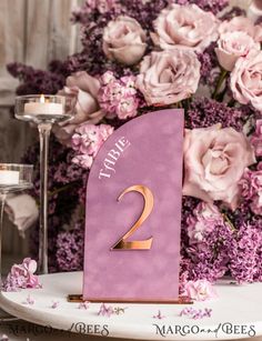 a purple table number sitting on top of a white plate next to pink flowers and candles