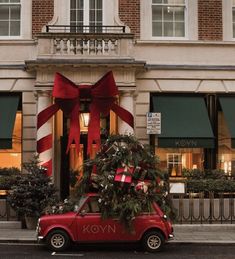 a red car parked in front of a building with a large christmas tree on top