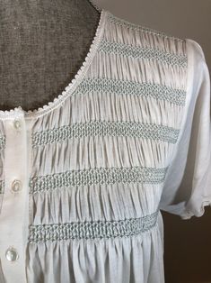 the back of a white blouse with green trims and buttons at the neckline