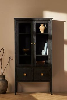 a black bookcase with glass doors and drawers in front of a vase on the floor