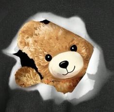 a brown teddy bear peeking out of a hole in the paper that has been torn open