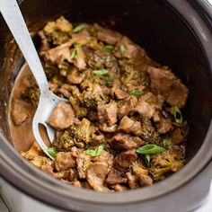 a slow cooker filled with meat and broccoli on top of a table