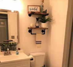 a white toilet sitting in a bathroom next to a sink and a wooden shelf above it