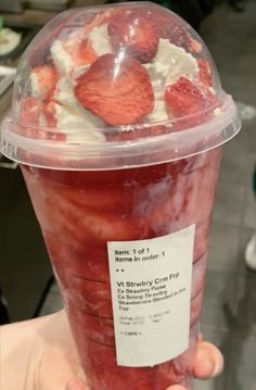 a plastic cup with strawberries and whipped cream in it is being held up by someone's hand