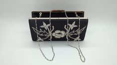 Add a touch of vintage glamour to your evening ensemble with this exquisite black satin clutch. The front of the clutch features beautiful silver embroidery in a floral and leaf design, accented with delicate sequins that catch the light. The back of the clutch is sleek and smooth, offering a refined look that complements any outfit. With a silver frame and clasp, this clutch provides a secure closure while maintaining a classic aesthetic. The interior is spacious enough to hold your essentials, such as a phone, keys, and lipstick, making it perfect for weddings, parties, or any special occasion. It also comes with a detachable silver chain strap, allowing you to wear it as a shoulder bag for hands-free convenience. This versatile clutch is an elegant accessory that adds a timeless touch o Lipstick Making, Satin Clutch, Silver Embroidery, Classic Aesthetic, Vintage Glamour, Silver Sequin, Elegant Accessories, Silver Frame, Clutch Handbag