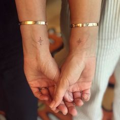 two people holding hands with cross tattoos on their wrist and fingers, both wearing gold bracelets