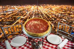 a deep dish pizza sits on top of a restaurant table overlooking the city at night