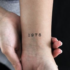 two hands holding each other with numbers tattooed on the wrist and one hand behind them