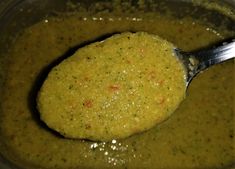 a spoon full of broccoli soup in a bowl with some sort of sauce