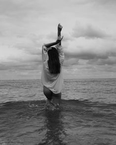 a woman standing in the ocean with her arms up