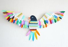 a colorful bird made out of colored crayons on a white wall with a blue tag hanging from it's side