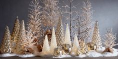 a group of christmas trees with snow on the ground and lights in the branches behind them