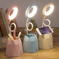 three different colored lights on top of a wooden table next to a phone and cactus