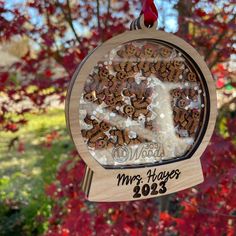 a wooden ornament hanging from a tree with red leaves in the back ground