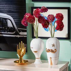 two white vases with flowers in them on a table next to a gold sculpture