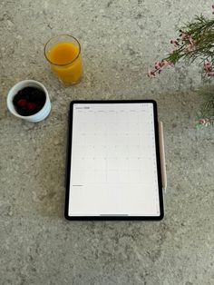 a tablet with a pen and a cup of orange juice next to it on a table