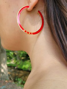 a woman wearing large red hoop earrings with the word babe written in gold on it