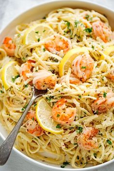 a white bowl filled with pasta and shrimp on top of a table next to lemon wedges