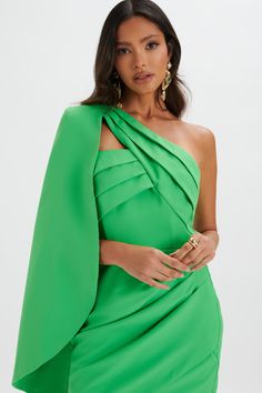 a woman wearing a green dress with an asymmetrical cape over her shoulders