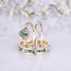 two gold rings with green and white stones on them, sitting next to each other