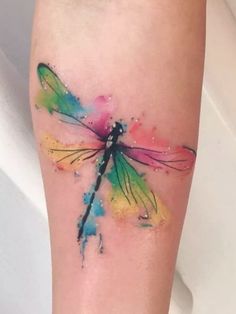 a colorful dragonfly tattoo on the left leg and right leg with watercolor paint splatters