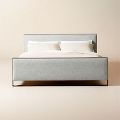 a bed with two pillows on top of it and a white blanket over the headboard