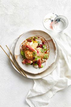 a white plate topped with food next to chopsticks and a glass of wine