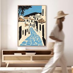 a woman in white is walking down the street with a hat on her head and a painting behind her