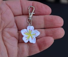 a hand holding a flower shaped keychain in it's left hand,