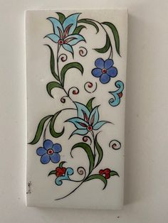 a white tile with blue flowers and green leaves on the bottom, against a white wall