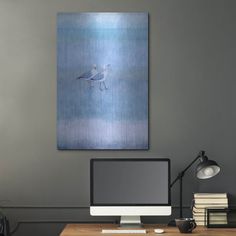 a desk with a computer, books and lamp on it in front of a gray wall