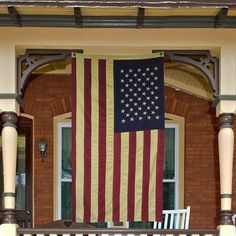 an american flag hanging from the side of a brick building on a porch with two chairs