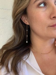 a woman in a white shirt is holding her hand up to her face and looking off into the distance