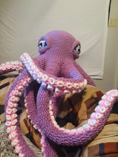 an octopus stuffed animal sitting on top of a bed covered in blankets and crochet