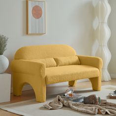 a yellow couch sitting on top of a wooden floor next to a white vase filled with flowers