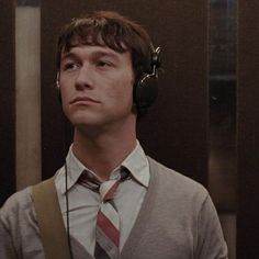 a man with headphones on standing in front of a mirror wearing a sweater and tie