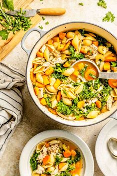 a pot filled with pasta and vegetables on top of a table next to a spoon