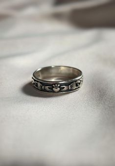 a silver ring with hearts on it sitting on top of a white cloth covered surface