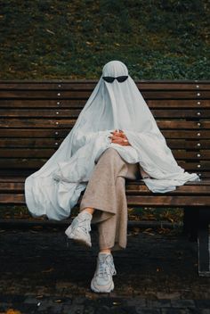 a person sitting on a park bench covered by a white cloth covering their face and head