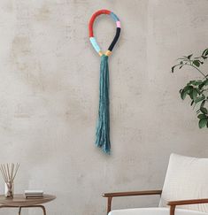 a wall hanging with tassels on it next to a chair and potted plant