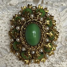 Dress up your winter coat or blazer or hat or scarf or handbag with this stunning Baroque style brooch. Green gems that emulate cats eye and faux pearls dance rings around each other to create depth and elegance.  Condition: Excellent Vintage. All of the items in the shop were previously loved and handled bringing with them the personal histories of the hands they have passed through. Sometimes this love shows up as extra wear and a few blemishes, sometimes it shows up as extreme care and nearly pristine condition. But all pieces have been around for well over 25 years, some closer to 100, so imperfections are expected and tend to add to the story of the item. All jewelry pieces are wiped clean but left unpolished as a bit of tarnish is preferred by many. With all vintage items, age-relate Elegant Green Oval Brooches, Elegant Brooch Pins For Vintage Events, Elegant Vintage Brooch Pins, Elegant Oval Brooch For Evening, Elegant Oval Evening Brooch, Elegant Oval Brooches For Evening, Elegant Oval Evening Brooches, Oval Brooches For Evening, Oval Evening Brooches