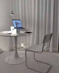 a laptop computer sitting on top of a table next to a white chair and lamp